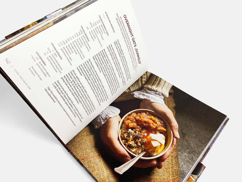 Open cookbook displaying autumn recipe with hands holding a bowl of savory dish topped with herbs.